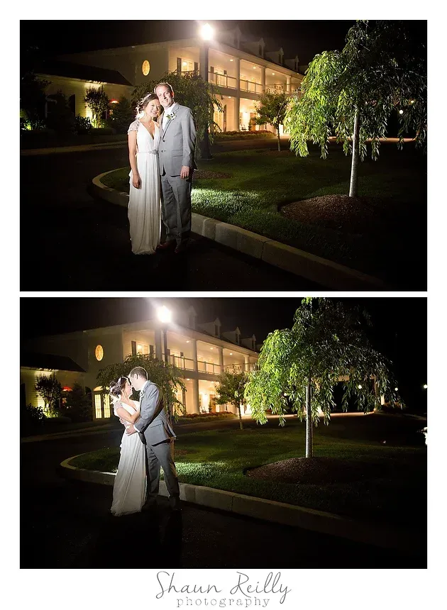 Couple in white wedding attire embracing outdoors at night in front of a lit building