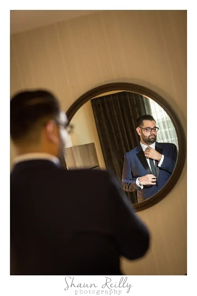 Man adjusting his tie while looking in a round mirror in a warm-toned room