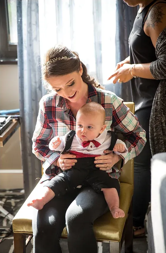 Woman holding a baby on her lap while another person stands nearby indoors