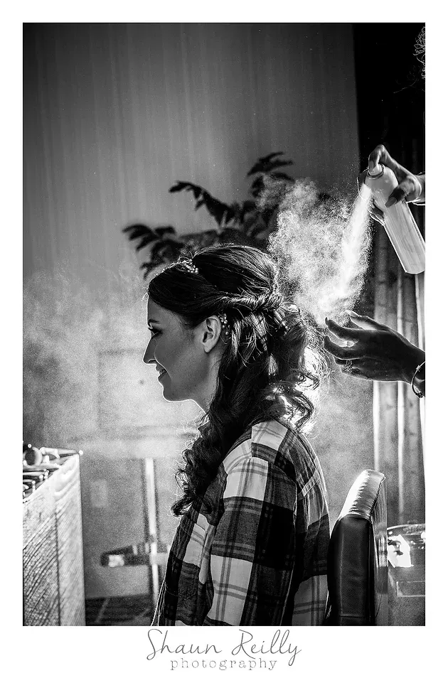 Black-and-white side-profile portrait of a person with feathers in their hair, indoors near a window.