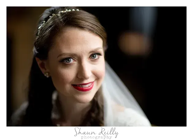 Smiling bride in a white veil with red lipstick, against a dark blurred background