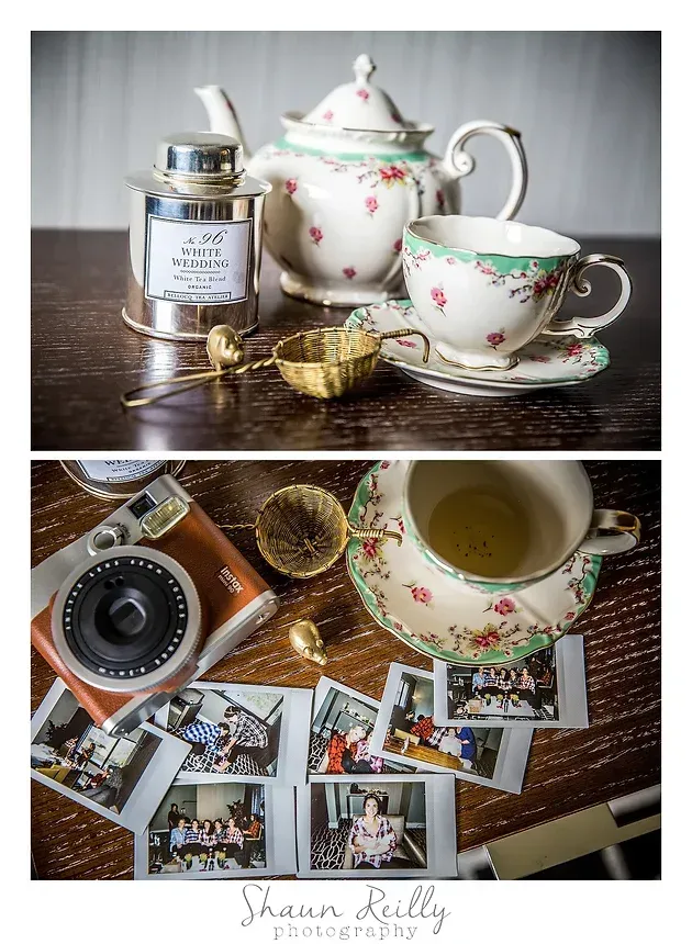 Vintage tea set with floral teapot, cups, and gold accents arranged on a table with photos and a camera