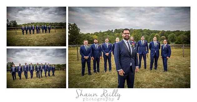 Wedding party in navy suits poses outdoors in a grassy field under cloudy skies.