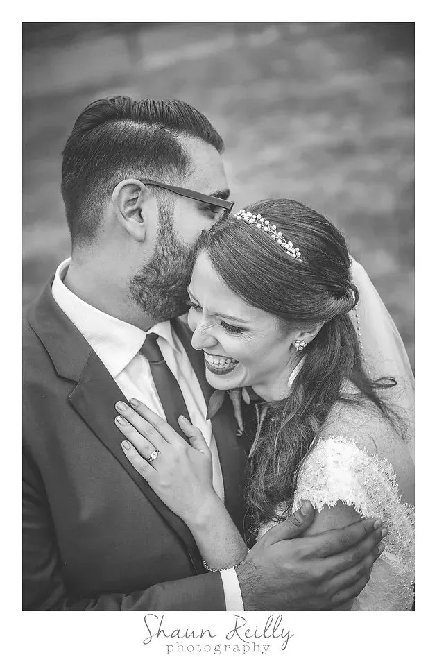 Couple in formal wear embracing and smiling in a black-and-white portrait outdoors