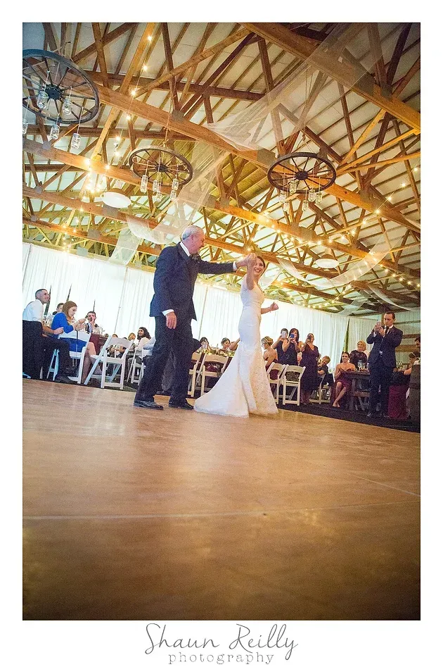 Bride and groom dancing in a rustic wedding hall with exposed wooden beams and seated guests