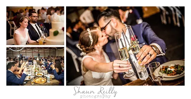 Wedding couple kissing at a reception table, with guests dining in the background