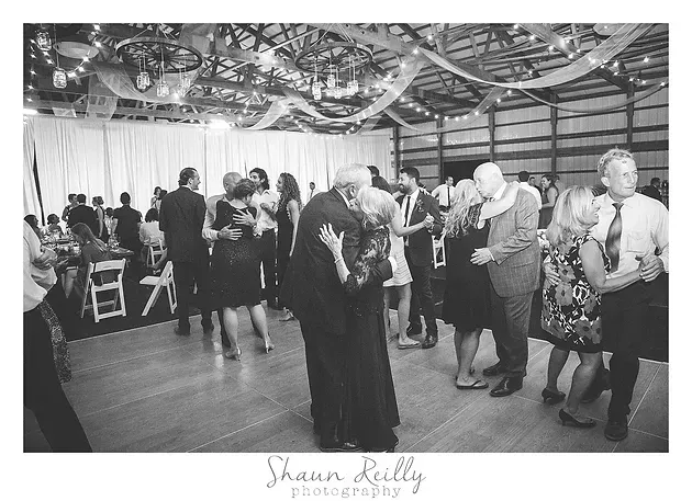 Guests dance at a decorated indoor wedding reception with draped ceiling ribbons.