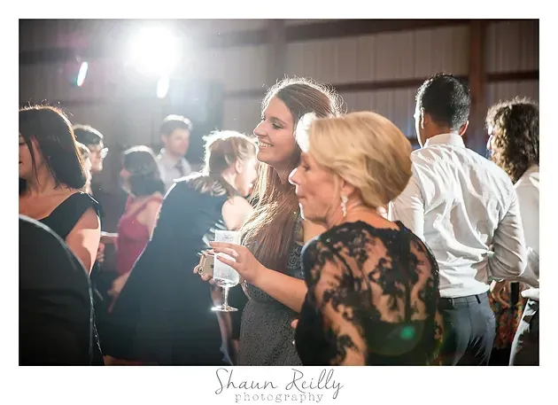 Guests mingling at a lively indoor reception, with a blonde woman holding a wine glass in the foreground.