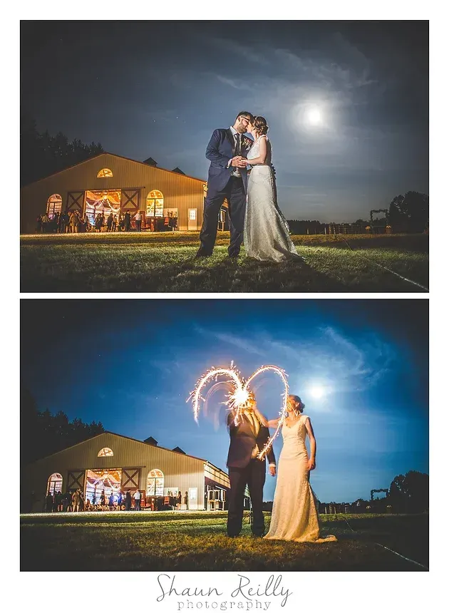 Wedding couple kissing outdoors at night, with sparkler trails and a lit barn in the background.