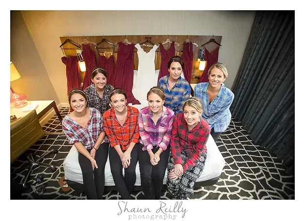 Seven people posing in front of a dressing room display with robes and hangers, smiling indoors.