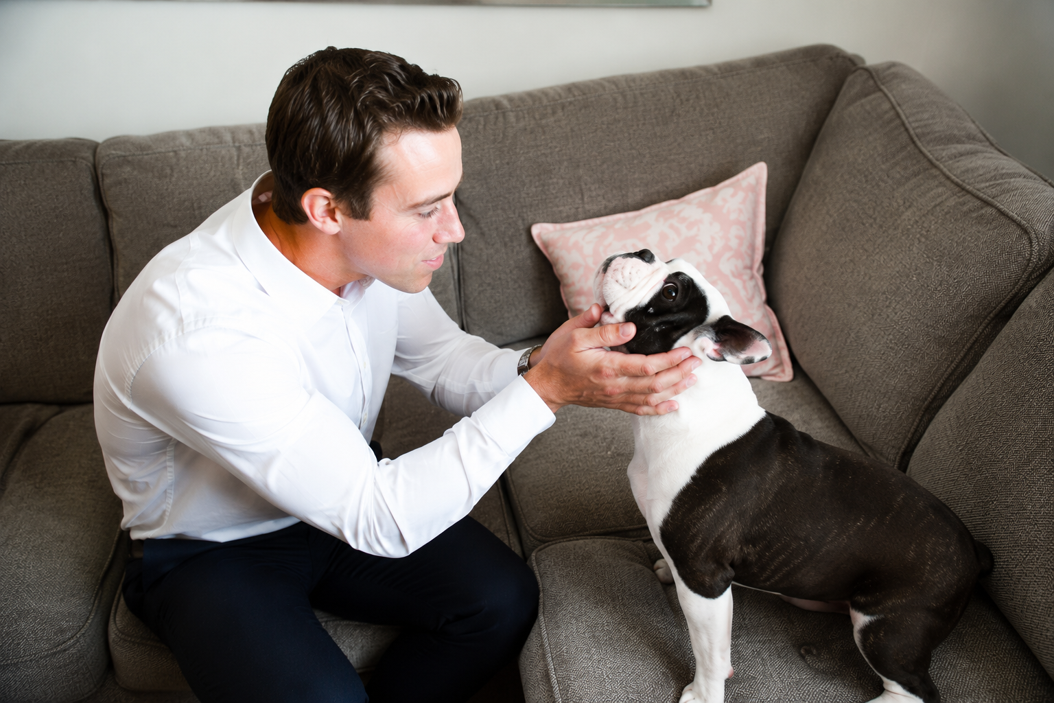 Man sitting on a couch gently petting a black-and-white dog indoors