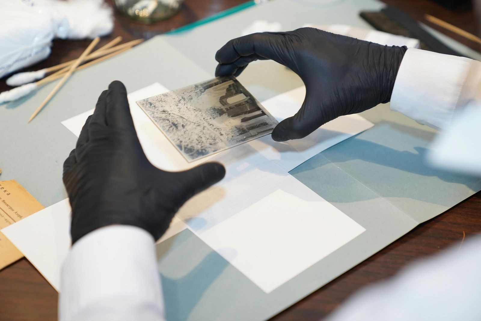 Gloved hands handling a clear film strip on a lab table with papers and test materials