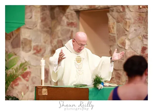 Priest in white robes speaking at an altar during a church service