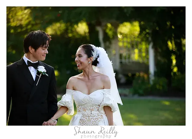 Bride and groom walking outdoors, smiling and holding hands in wedding attire