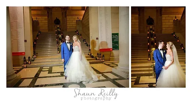 Bride and groom pose in a grand stairway lobby beside a decorated Christmas tree.