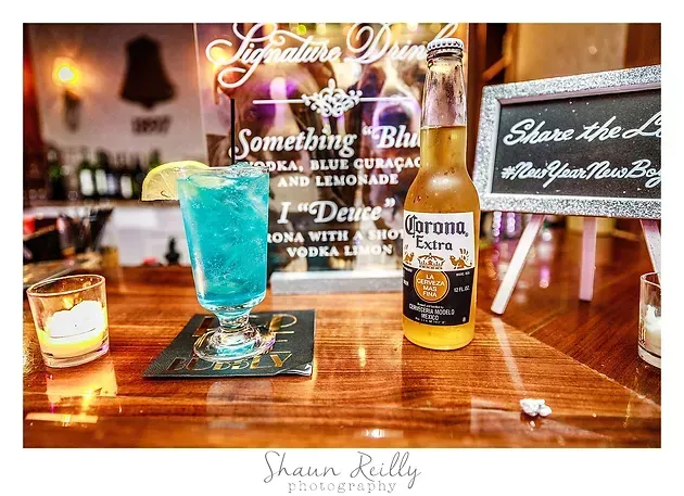 Blue cocktail and Corona beer on a wooden bar with candlelight and menu signs in the background