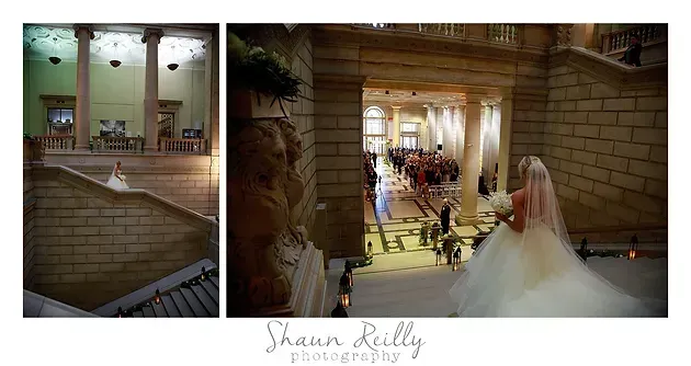 Wedding couple in a stone hall, with an indoor balcony view and a bride and groom walking below