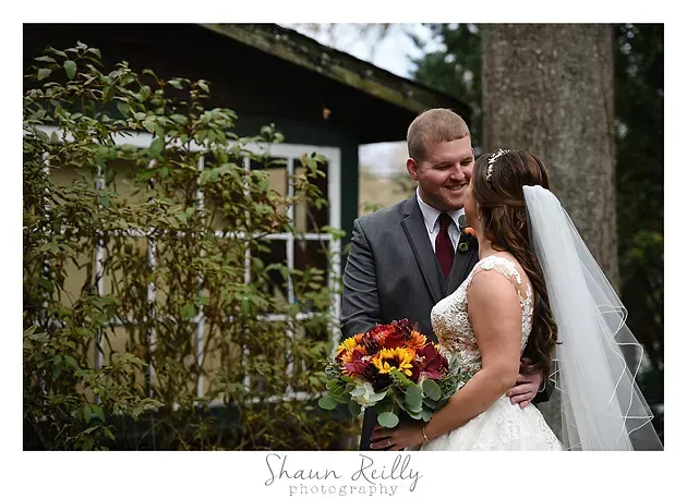Bride and groom smiling outdoors by a rustic building, holding a colorful bouquet