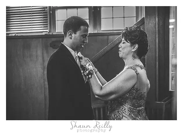 Two people in formal dress stand close in a wood-paneled room, speaking face to face.