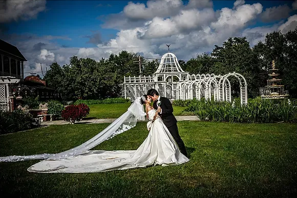 Bride and groom kissing in a garden, with a long white gown train and decorative white arches behind them