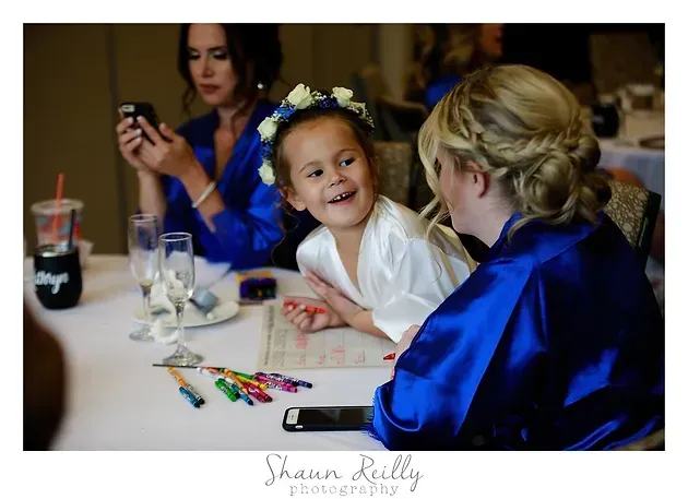 Children in blue robes smiling at a table with face-paint supplies and a smartphone nearby