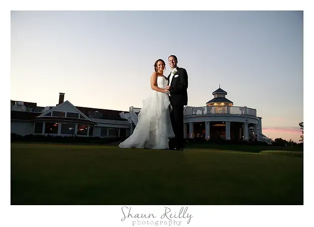 Bride and groom posing on a lawn at sunset in front of a clubhouse