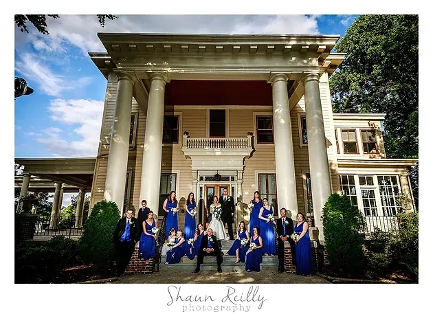 Graduation group posed on mansion steps with columns, wearing blue gowns and holding bouquets