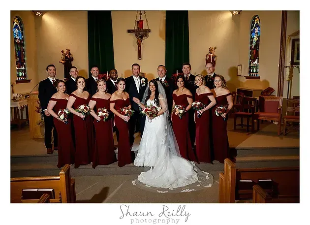 Bridal party posed in a church, with bride in white centered among attendants in burgundy dresses