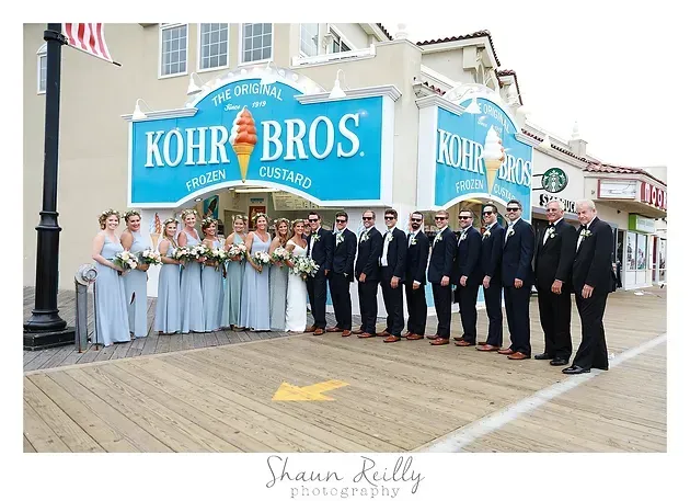 Group posing on boardwalk in front of Kohr Bros. building, with bridesmaids, groomsmen, and wedding party in formal attire