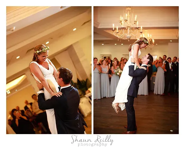 Bride and groom dancing and lifting together at a wedding reception in a warmly lit ballroom.