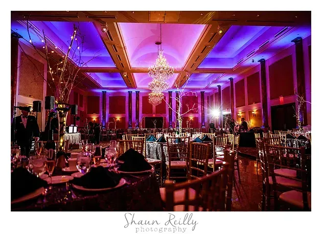 Elegant banquet hall lit in purple and pink with chandeliers and set dining tables