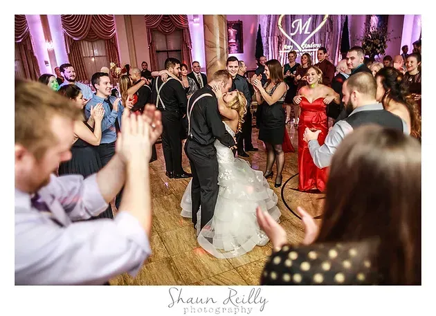 Bride and groom dance amid cheering guests at a wedding reception in a decorated ballroom