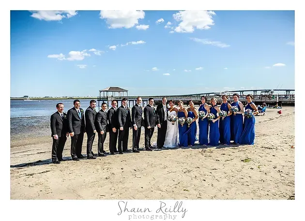 Wedding party posed on a sandy beach with ocean and pier in the background