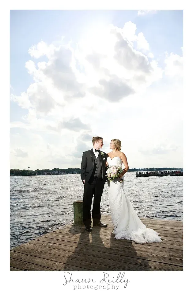 Bride and groom standing by the water under a cloudy sky