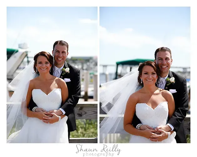 Wedding couple posing outdoors by the water, smiling in a white dress and dark suit.