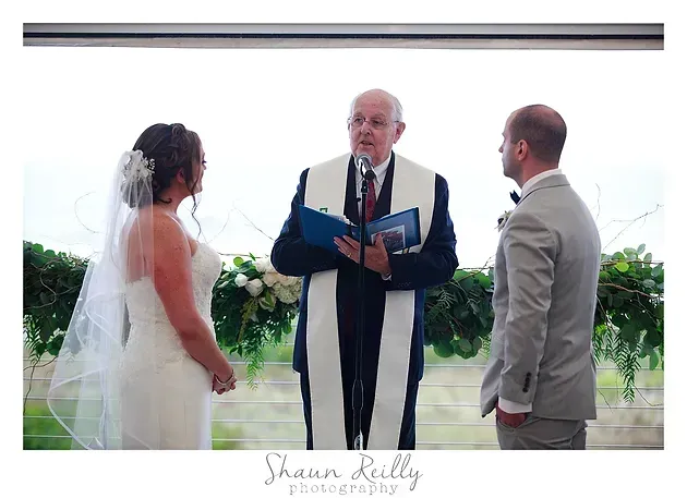 Bride and groom stand before an officiant during an outdoor wedding ceremony