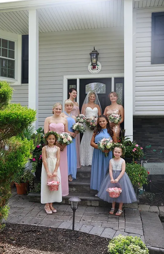 Wedding party posing on a porch in pastel dresses, holding bouquets.