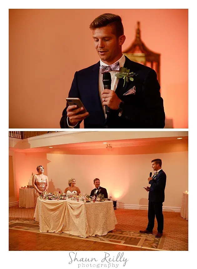 Man in a dark suit giving a toast at a warm-lit wedding reception, with guests seated nearby.