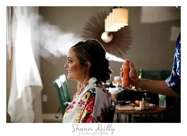 Woman getting hair sprayed in a salon, smiling in profile with steam or spray visible.