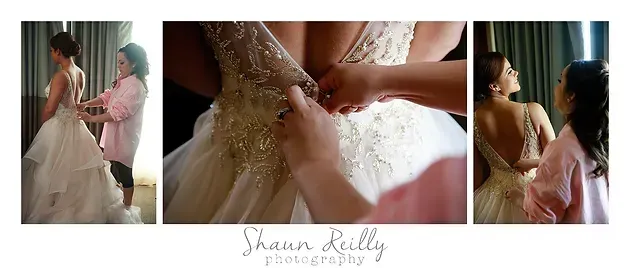 Bride getting dressed in a white wedding gown, assisted by another person in a softly lit room.