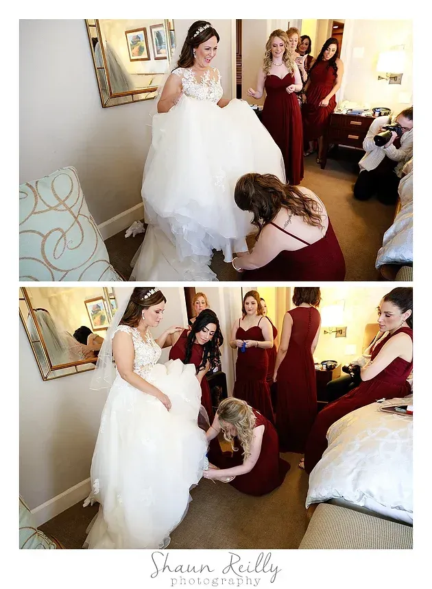 Bride in white dress with bridesmaids helping arrange her gown in a bedroom