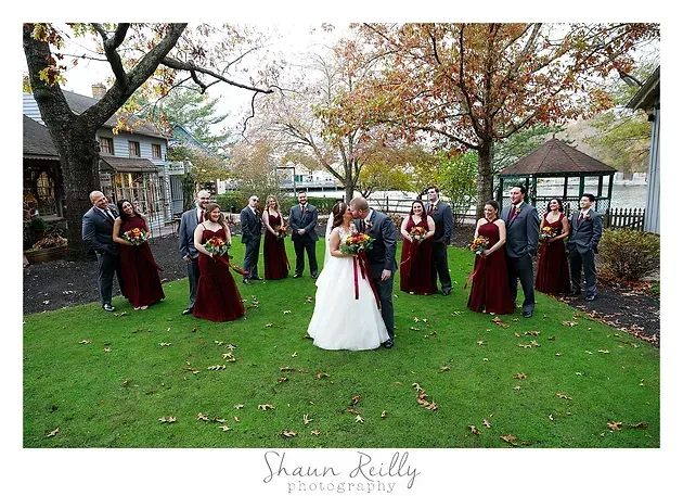 Bride and bridesmaids in burgundy dresses posing outdoors on a lawn in autumn