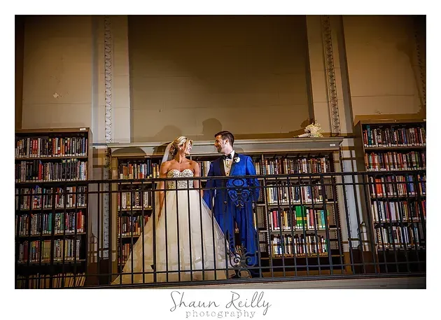 Bride and groom standing together in a library, holding hands and smiling