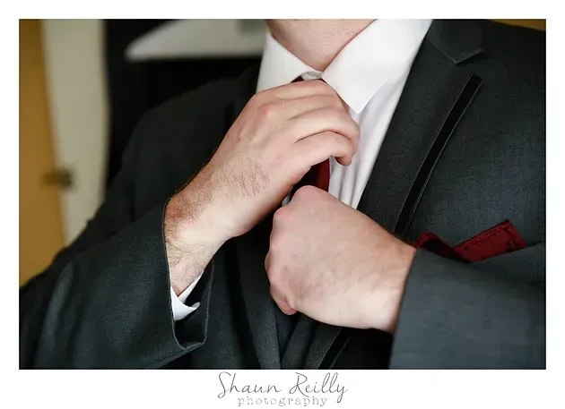 Man adjusting white tie with a dark suit and red pocket square