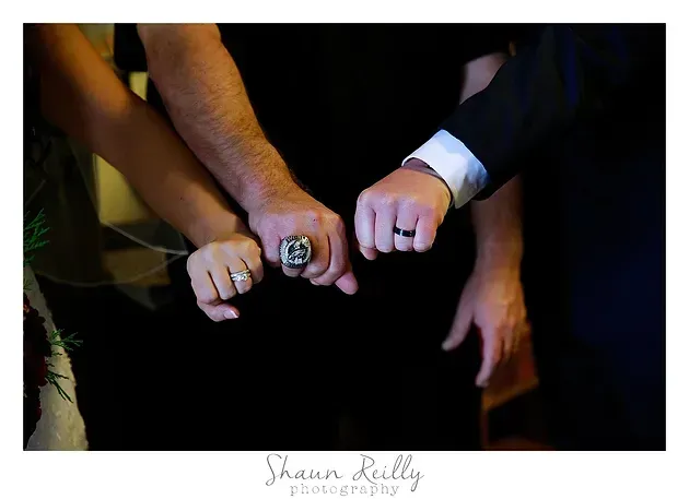 Hands with rings and a suit cuff linked together in a dark, formal setting