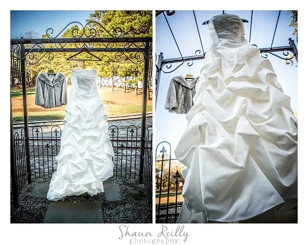 White ruffled wedding dress hanging on an ornate black gate outdoors in a garden; close-up detail view.