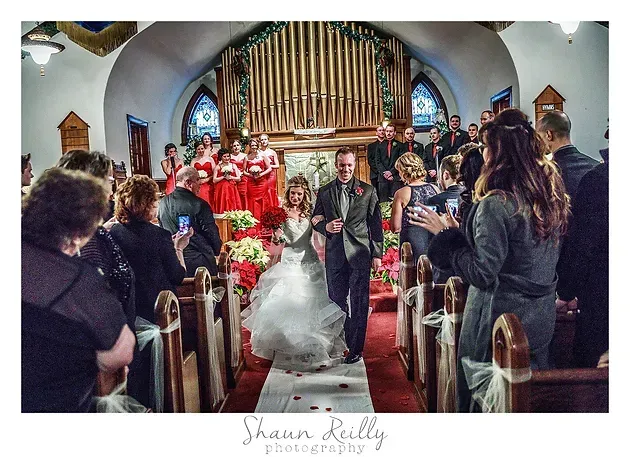 Wedding couple walking down church aisle, guests standing, with choir and organ in the background.