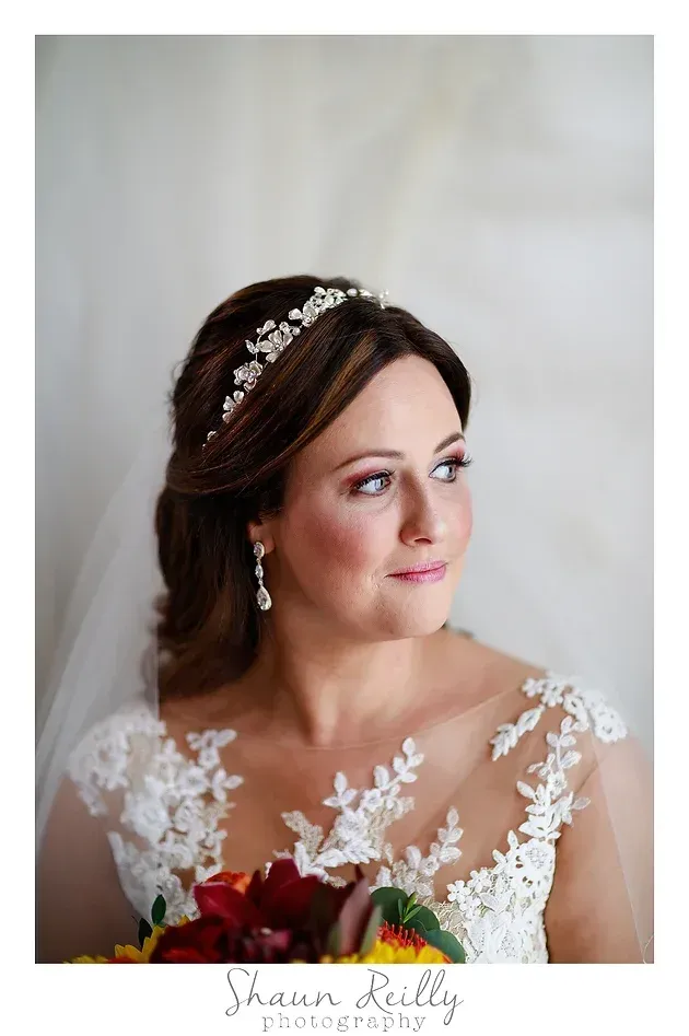 Bride in a white lace gown and veil, holding a bouquet, gazing to the side.