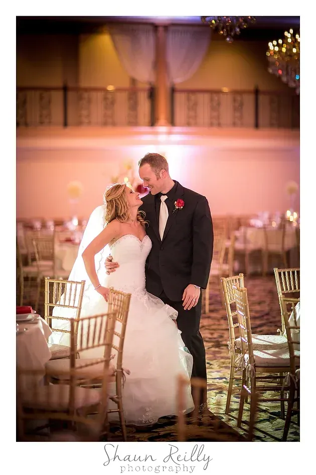 Bride and groom kissing at a wedding reception beside gold chairs and warm pink lighting