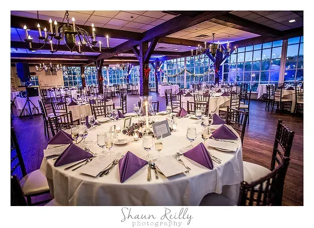 Elegant banquet hall with round, white-clothed tables set for a formal event, lit in purple and blue
